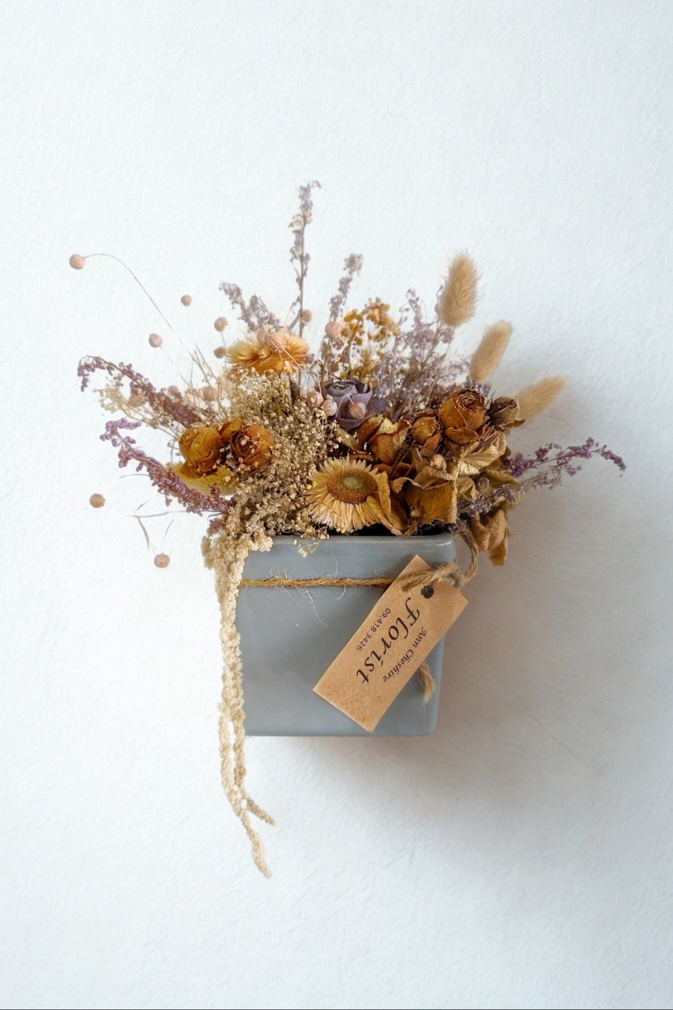 Dried flower arrangement in a small box with a tag on a white background
