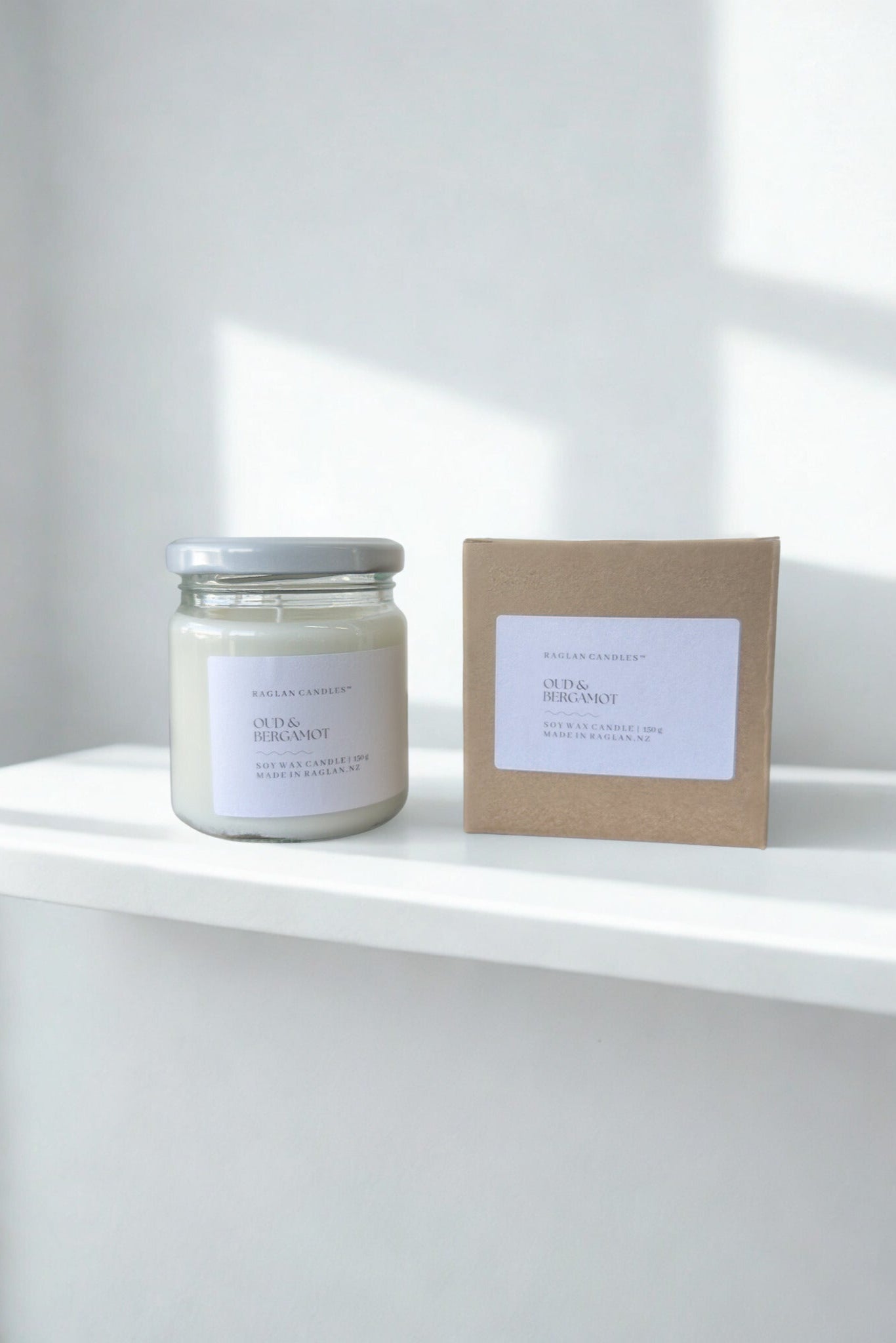 Candle and its packaging on a white surface with a light gray background