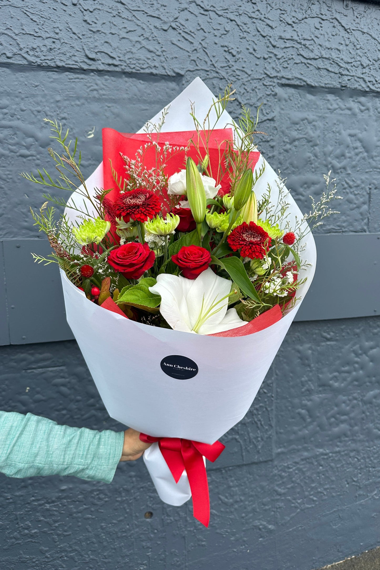 Bouquet of red and white flowers with a red ribbon held against a gray wall.