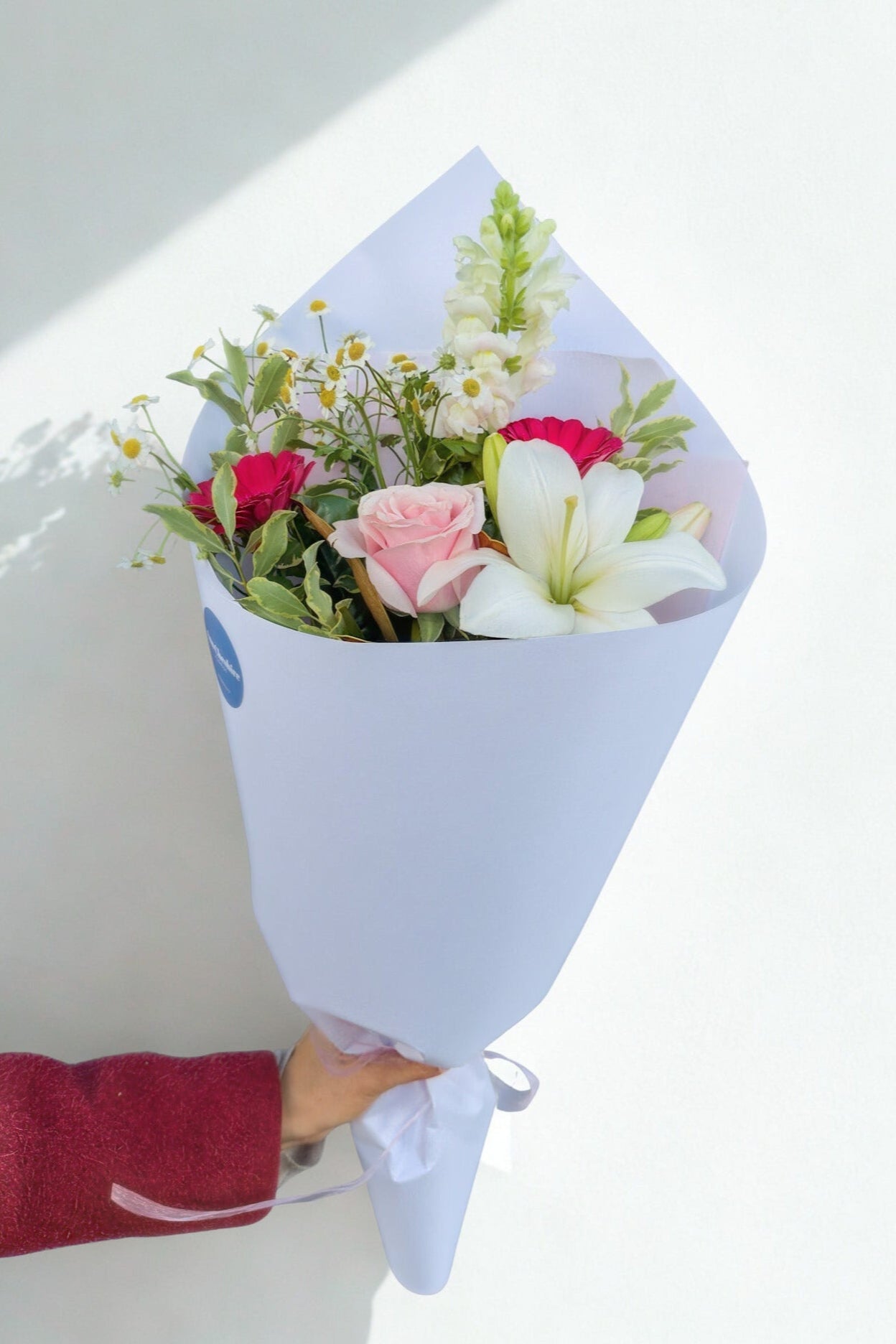 Bouquet of flowers wrapped in white paper held by a person with a red sleeve.