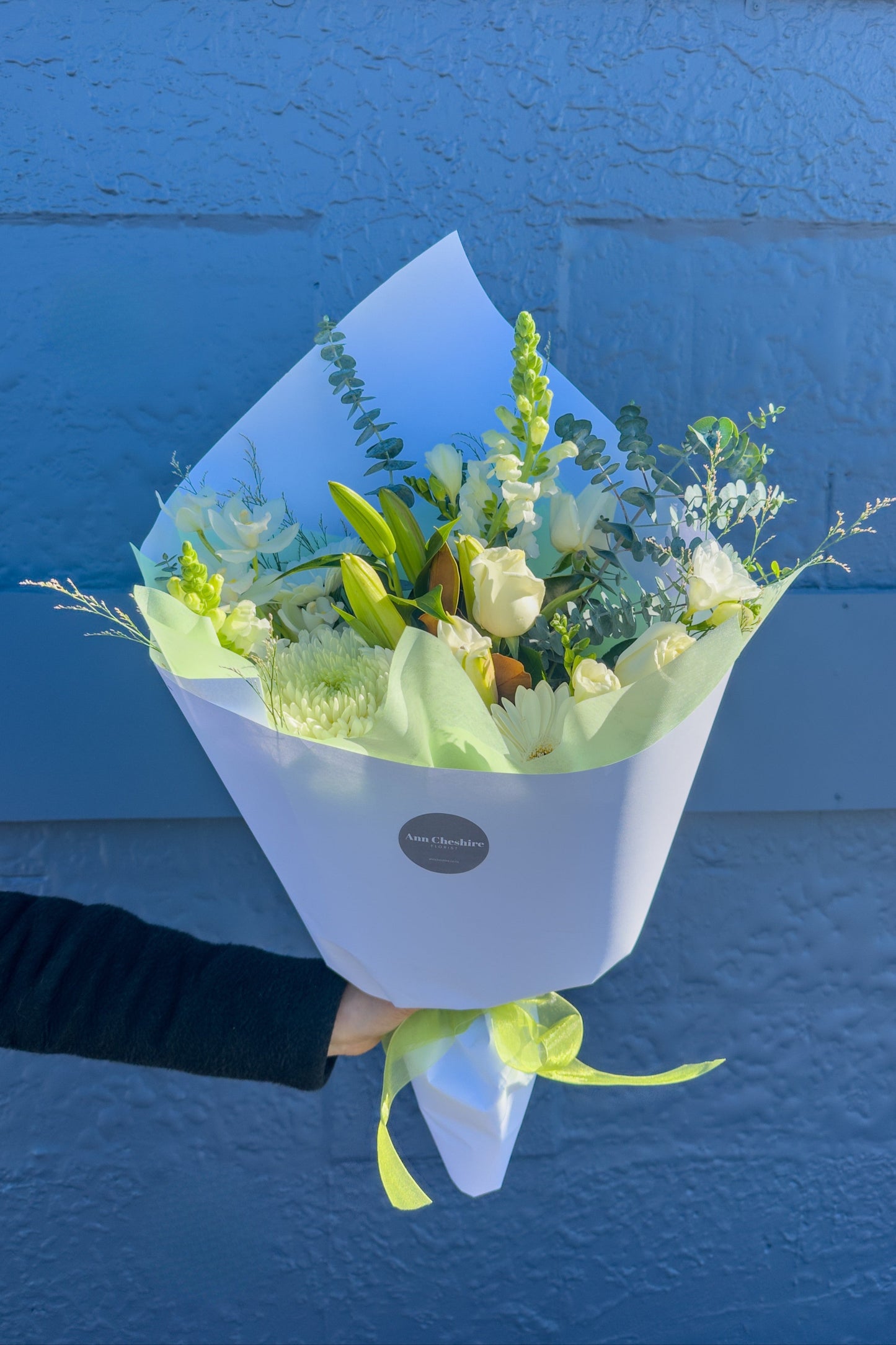 Bouquet of flowers wrapped in white paper with a green bow against a blue background