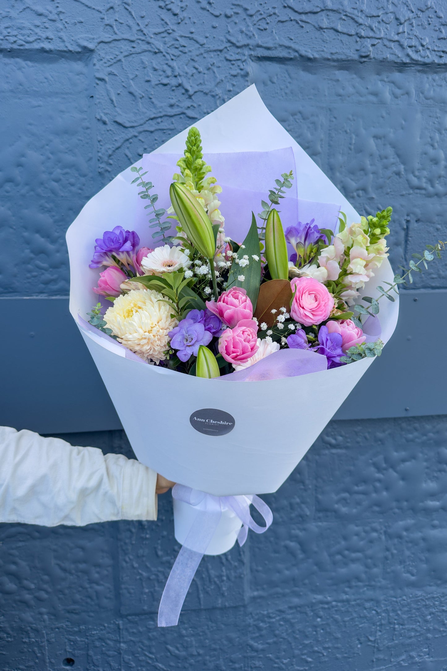 Bouquet of flowers held against a blue wall