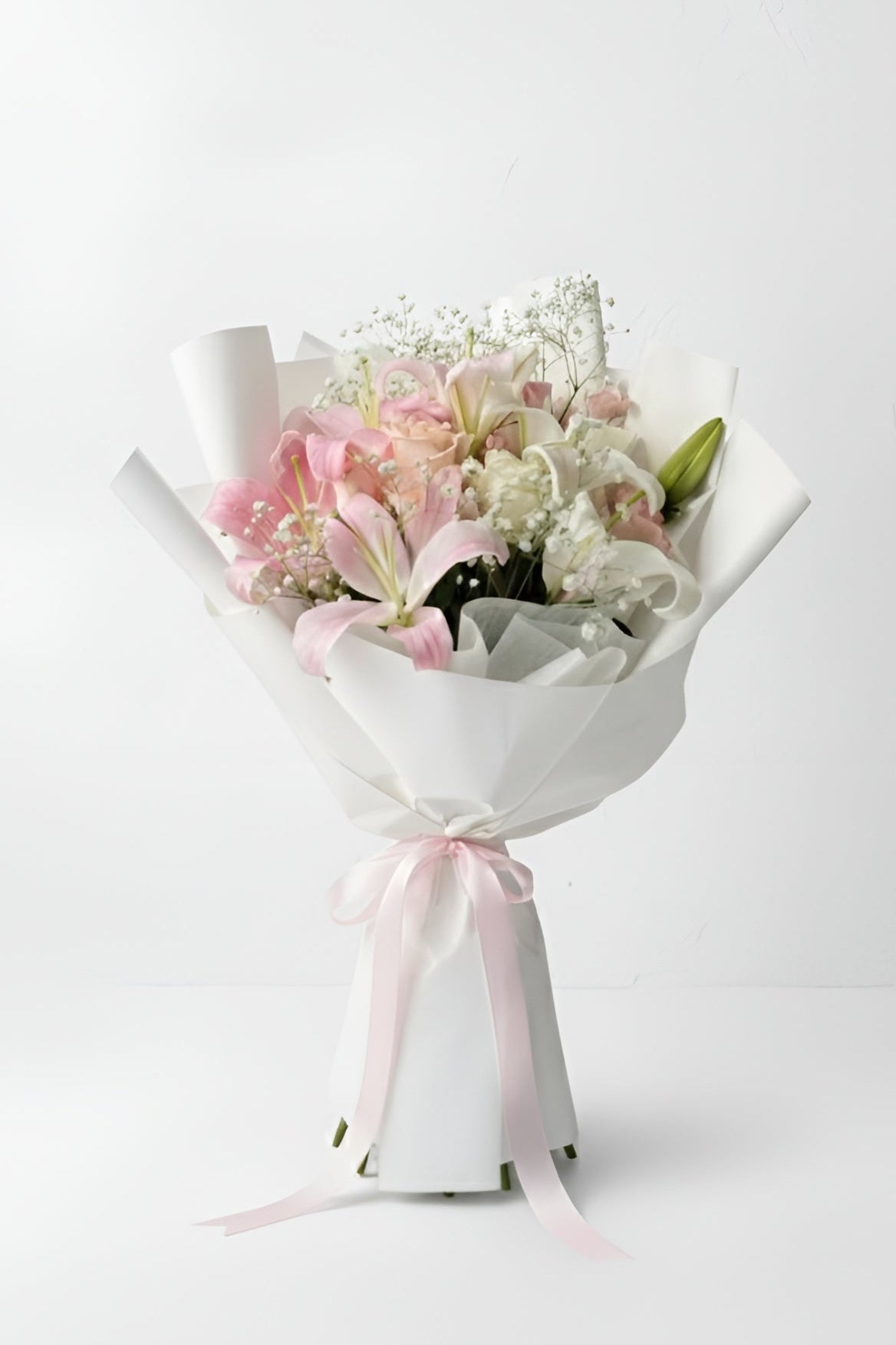 Bouquet of flowers wrapped in white paper with a pink ribbon on a white background
