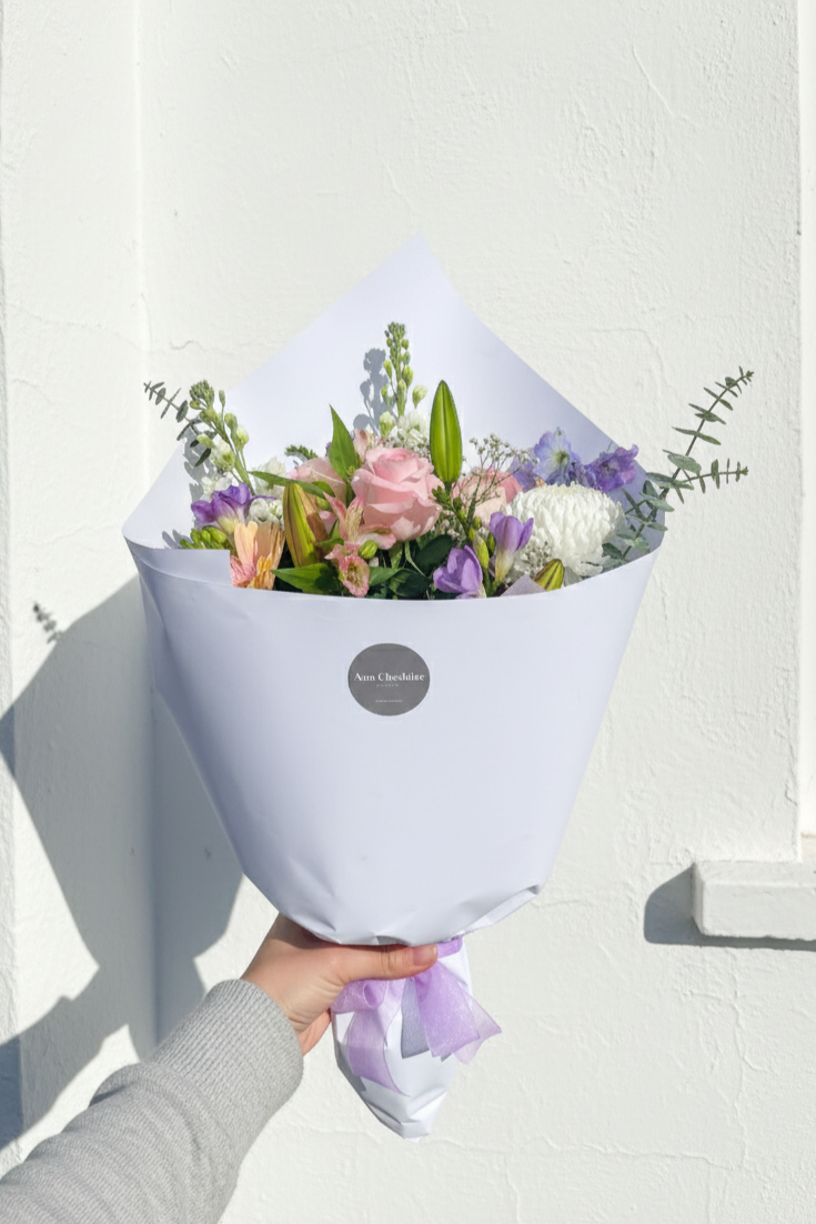 Bouquet of flowers wrapped in white paper held against a white wall.