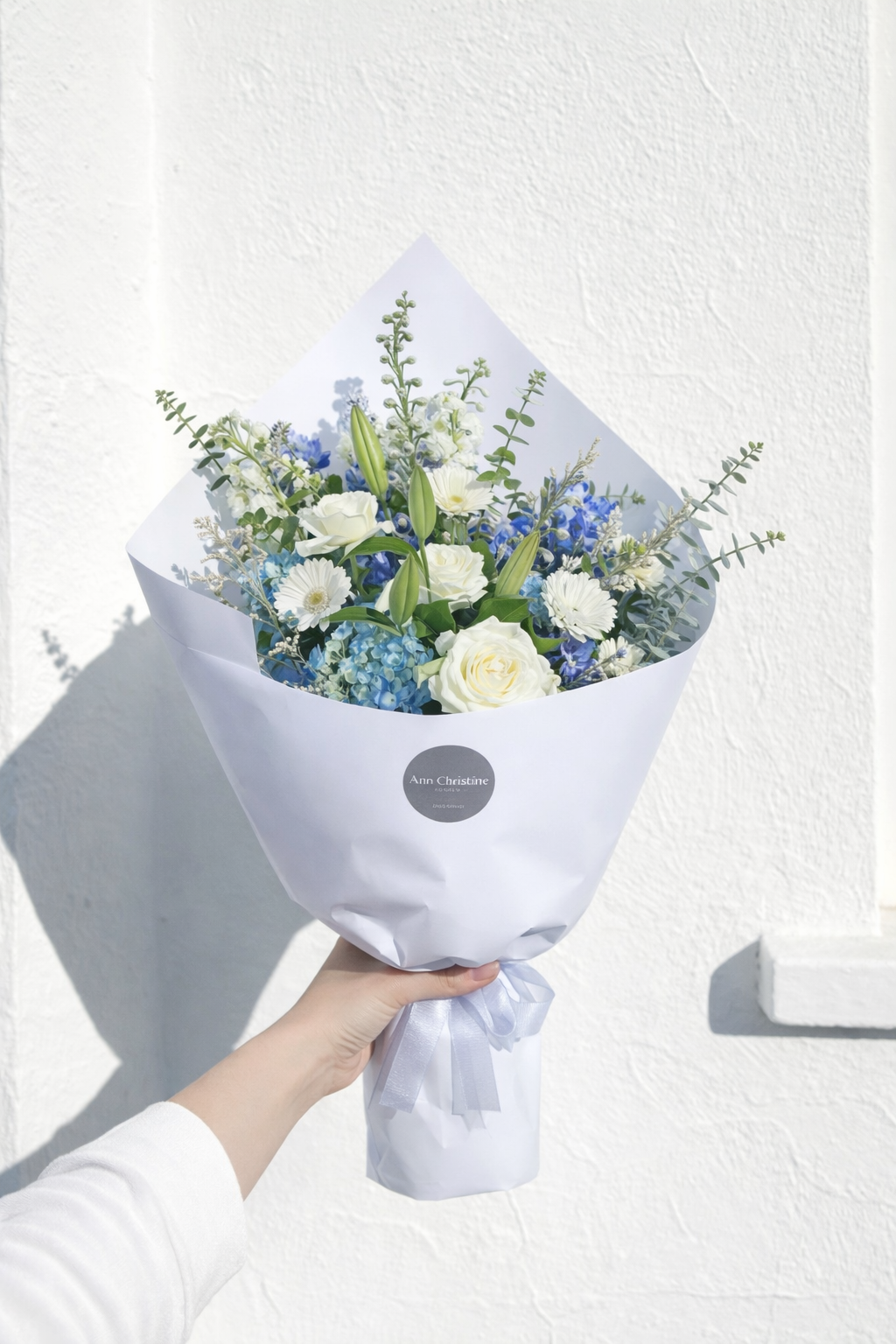 Bouquet of flowers wrapped in white paper held by a person against a light background