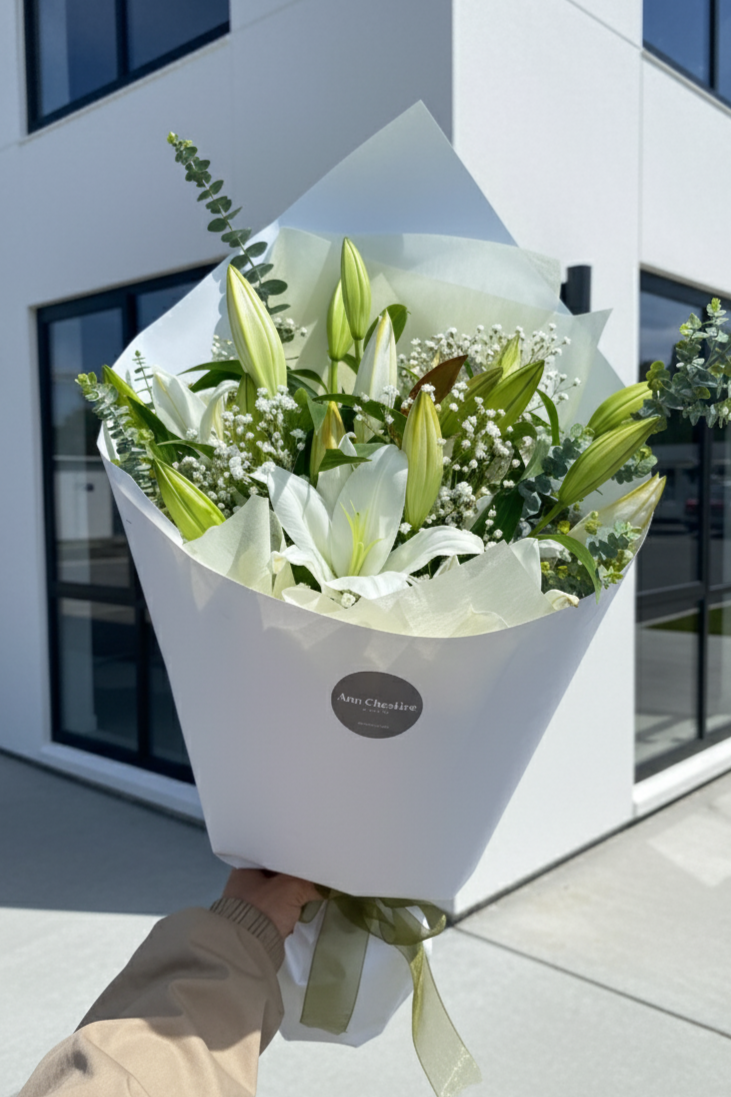 Bouquet of white flowers with green leaves held in front of a modern building.