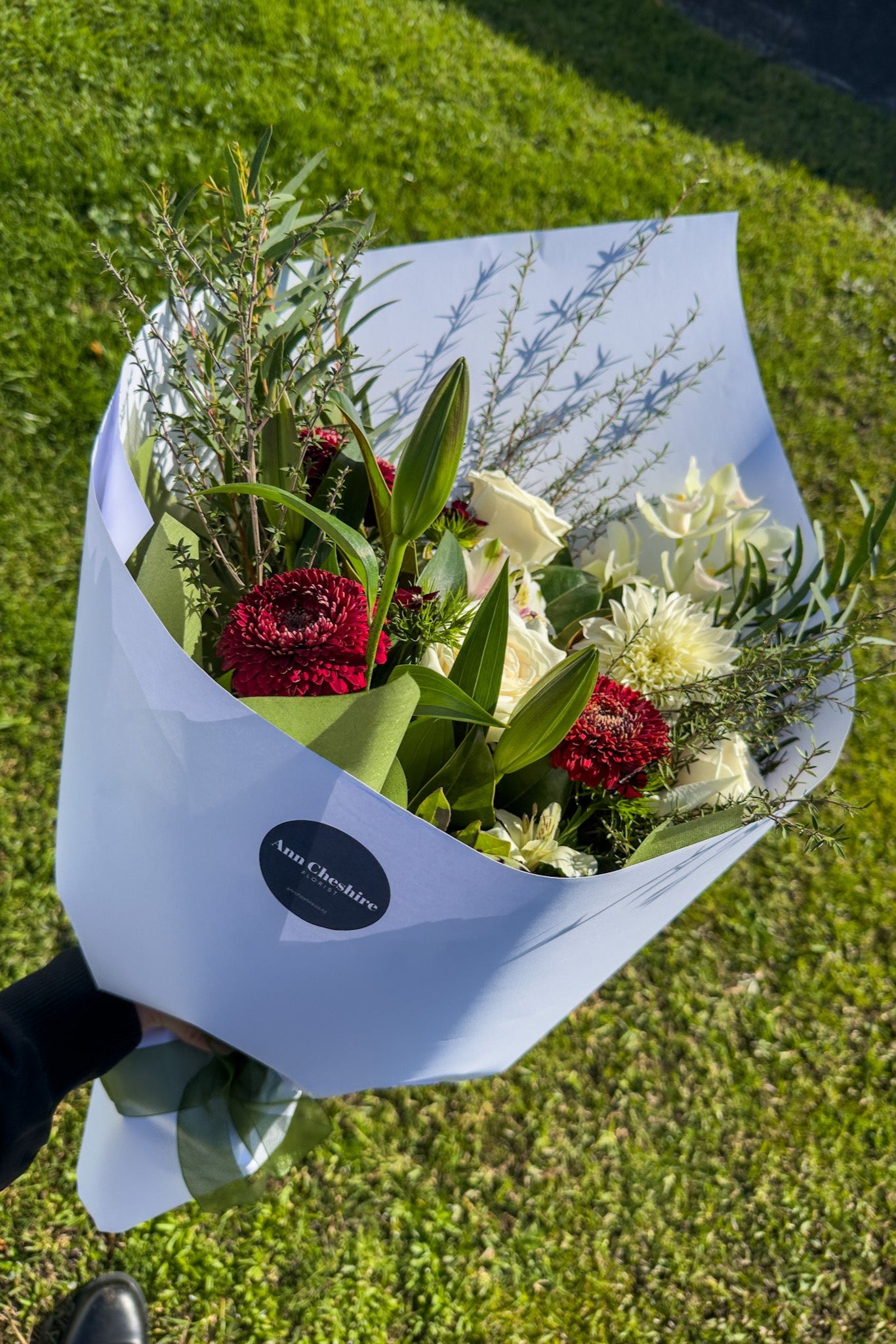 Bouquet of flowers wrapped in white paper held by a person on grass