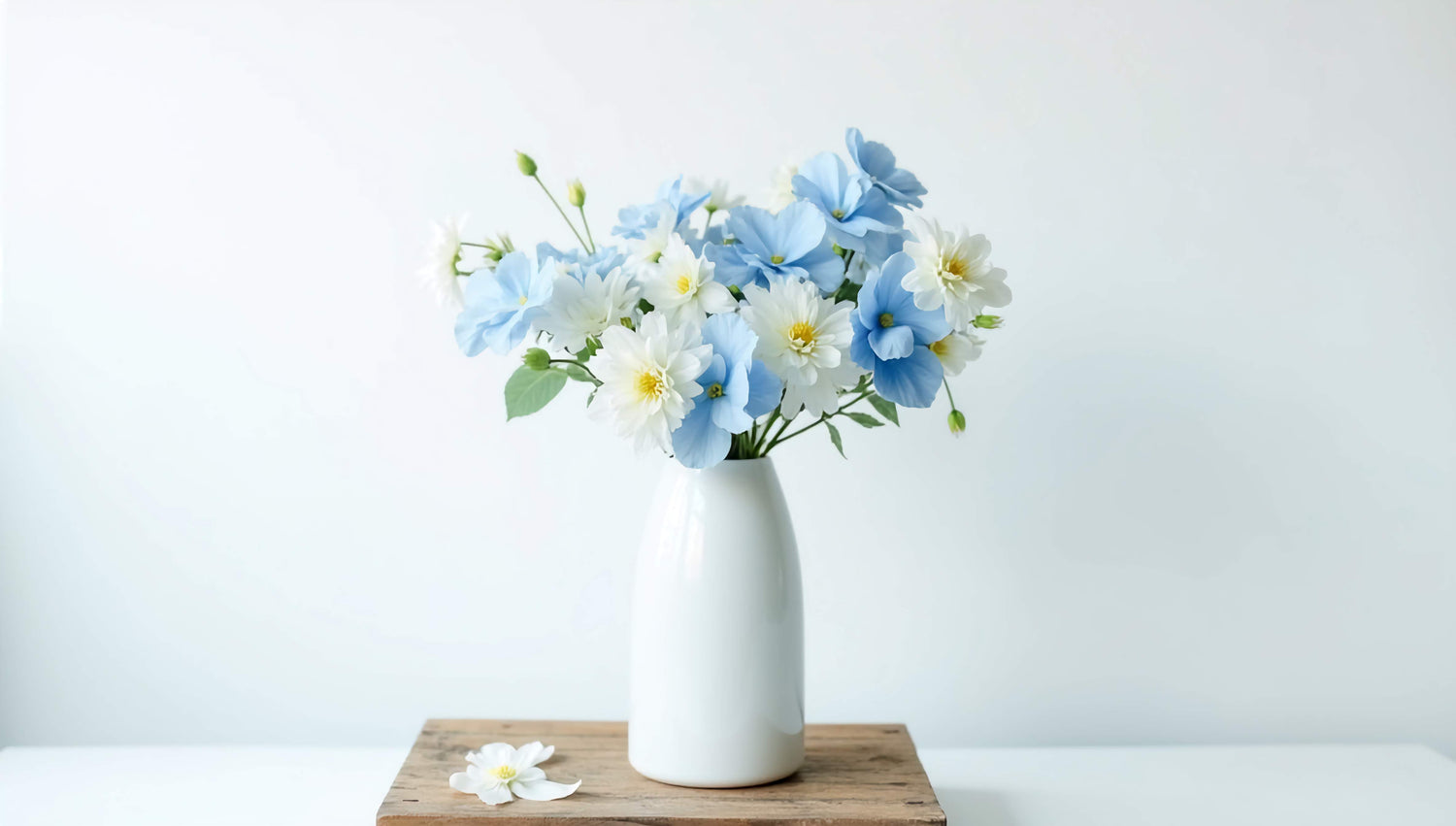 A delicate arrangement of blue and white flowers in a white vase placed on a wooden surface against a minimalistic background.