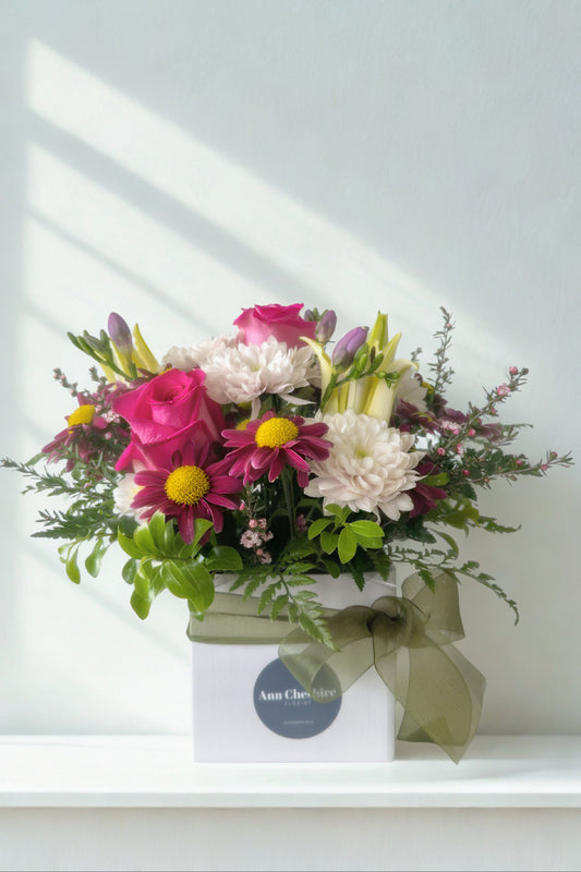 Colorful flower arrangement in a box on a white surface with a light gray background