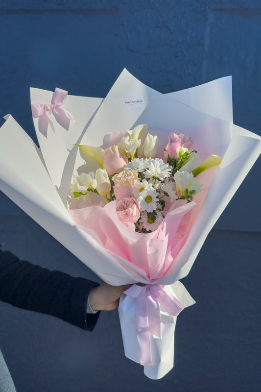 Bouquet of flowers wrapped in white paper with pink ribbons against a blue background