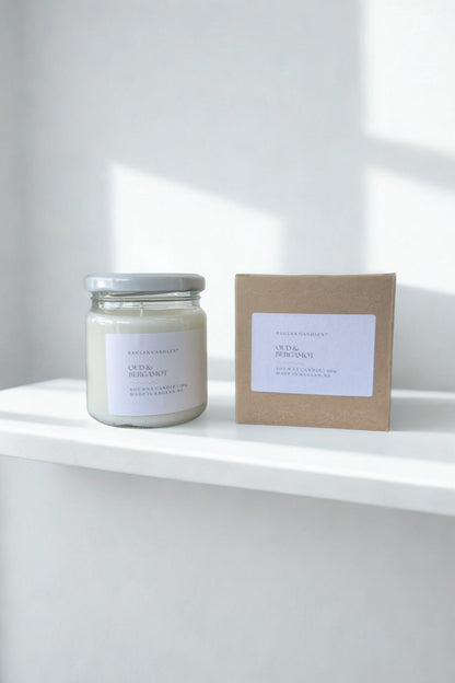 Candle and its packaging on a white surface with a light gray background