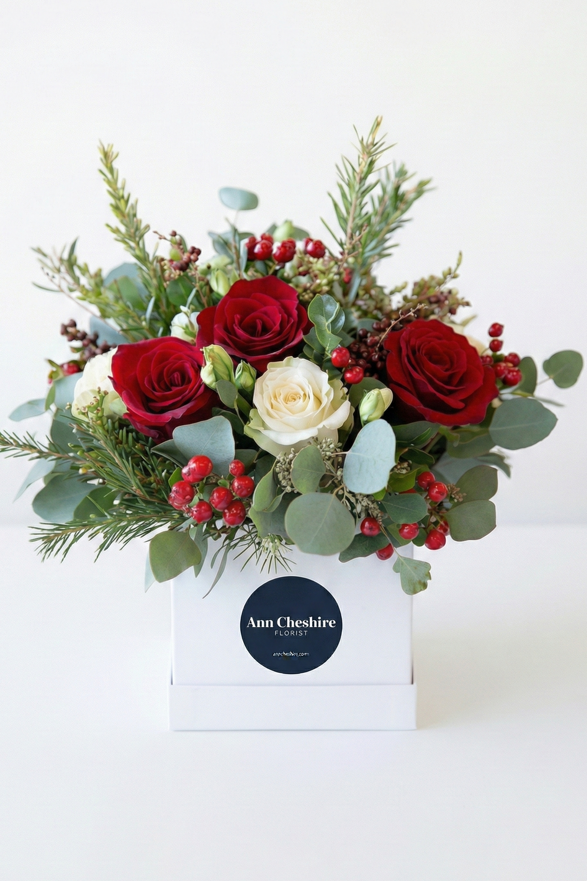 Bouquet of red and white flowers with greenery in a box on a white background