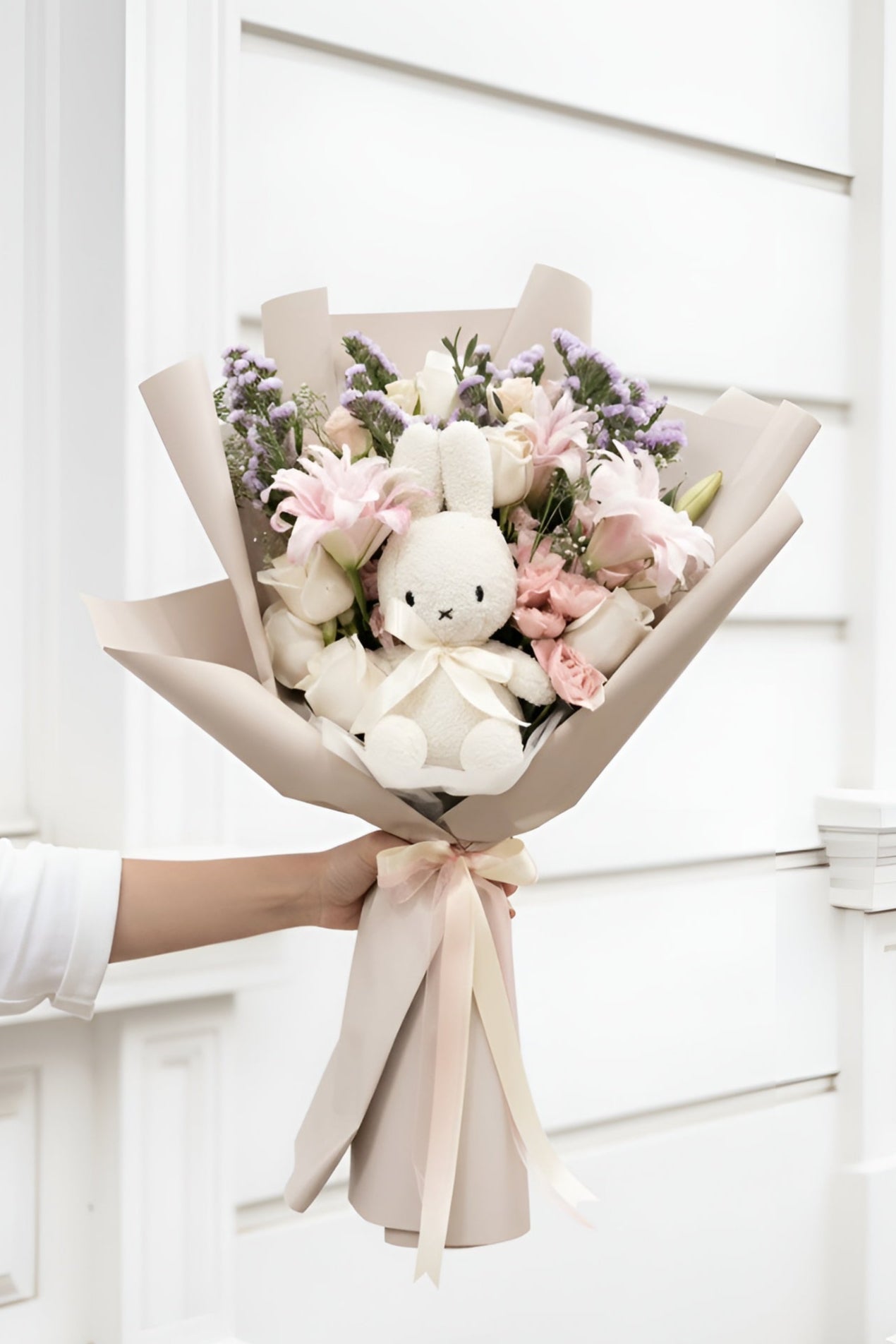 Bouquet of flowers with a plush toy held by a person in front of a white door.