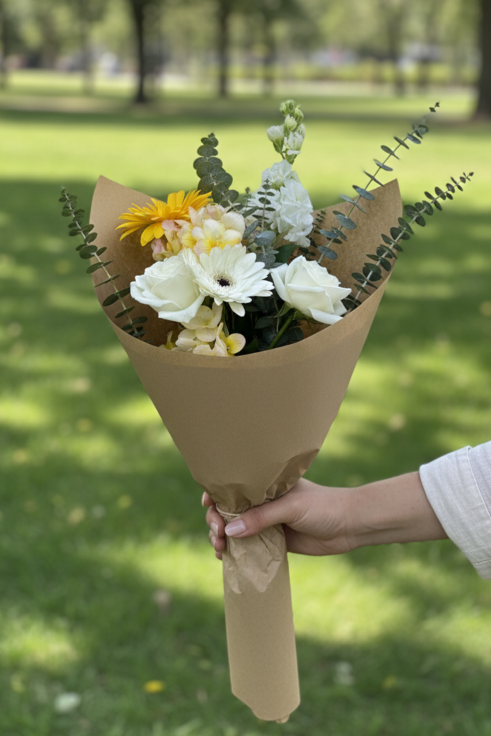 Bouquet of flowers wrapped in brown paper held by a person in a park.