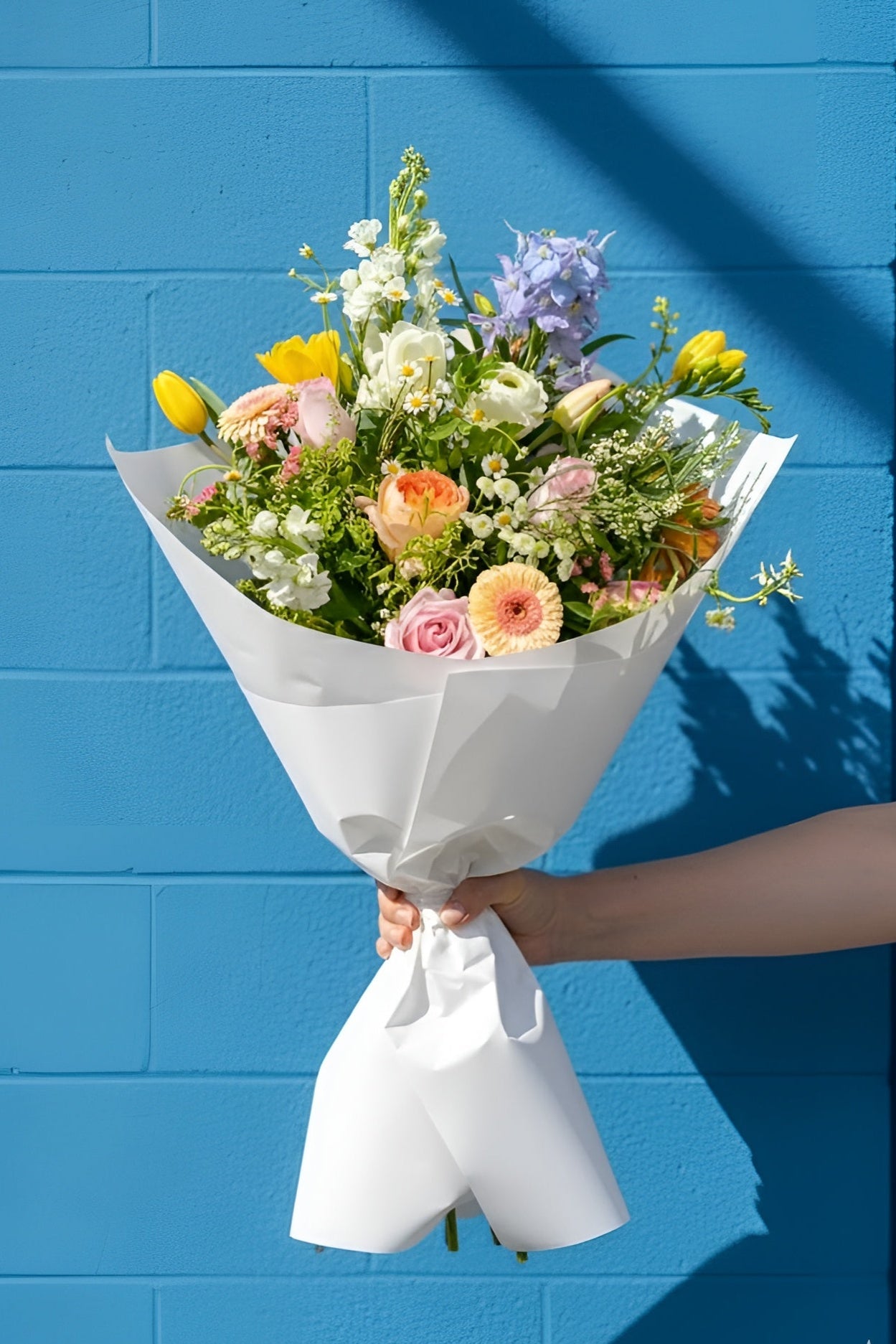 Bouquet of flowers held against a blue brick wall