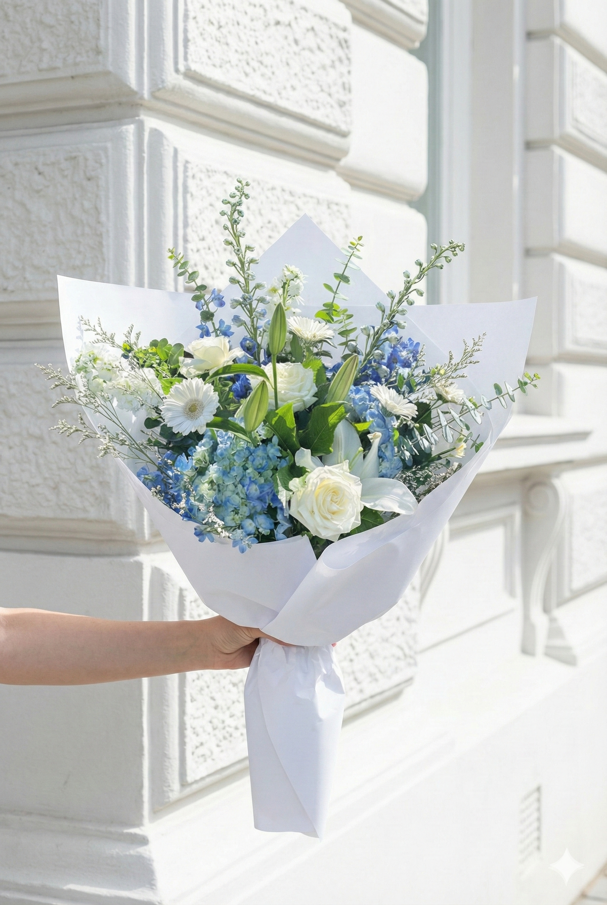 Bouquet of flowers held by a person in front of a white decorative wall.