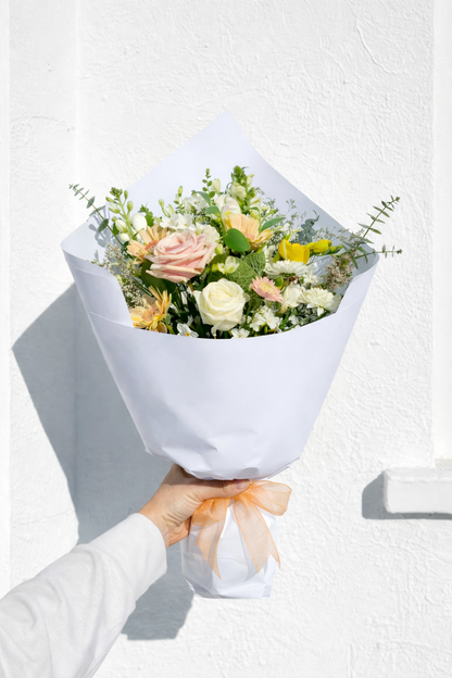 Bouquet of flowers wrapped in white paper held by a person against a light background
