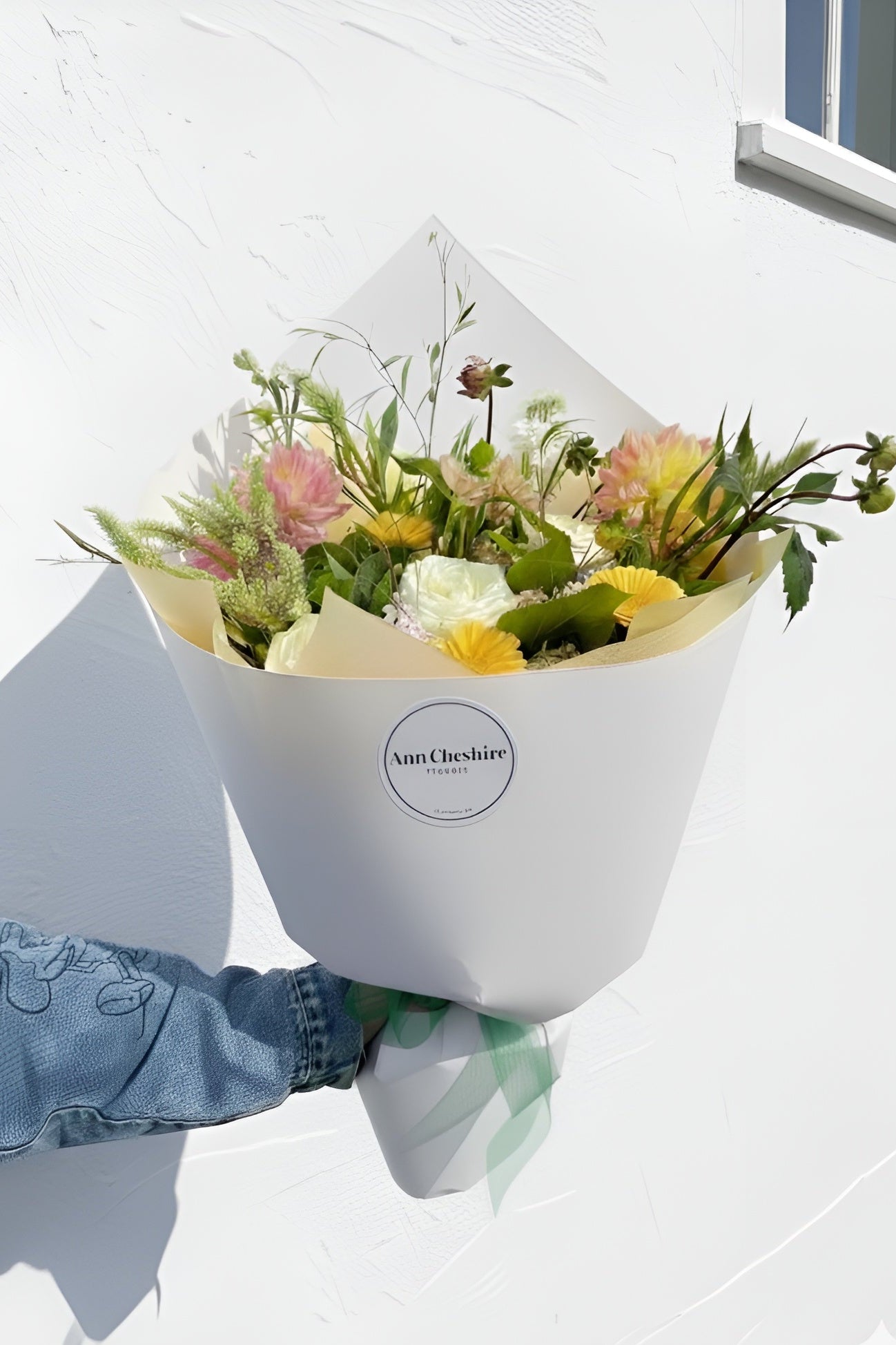 Bouquet of flowers held by a person wearing a blue jacket against a white background