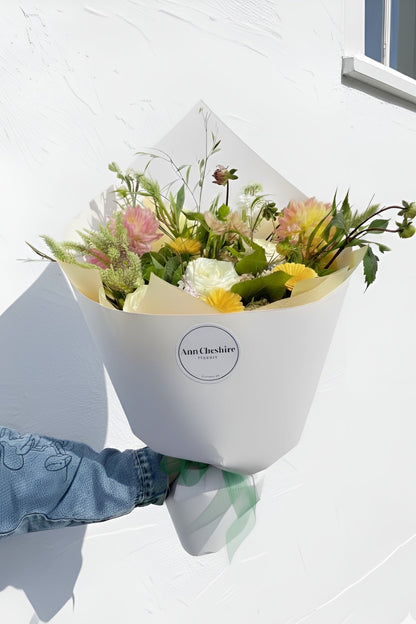Bouquet of flowers held by a person wearing a blue jacket against a white background