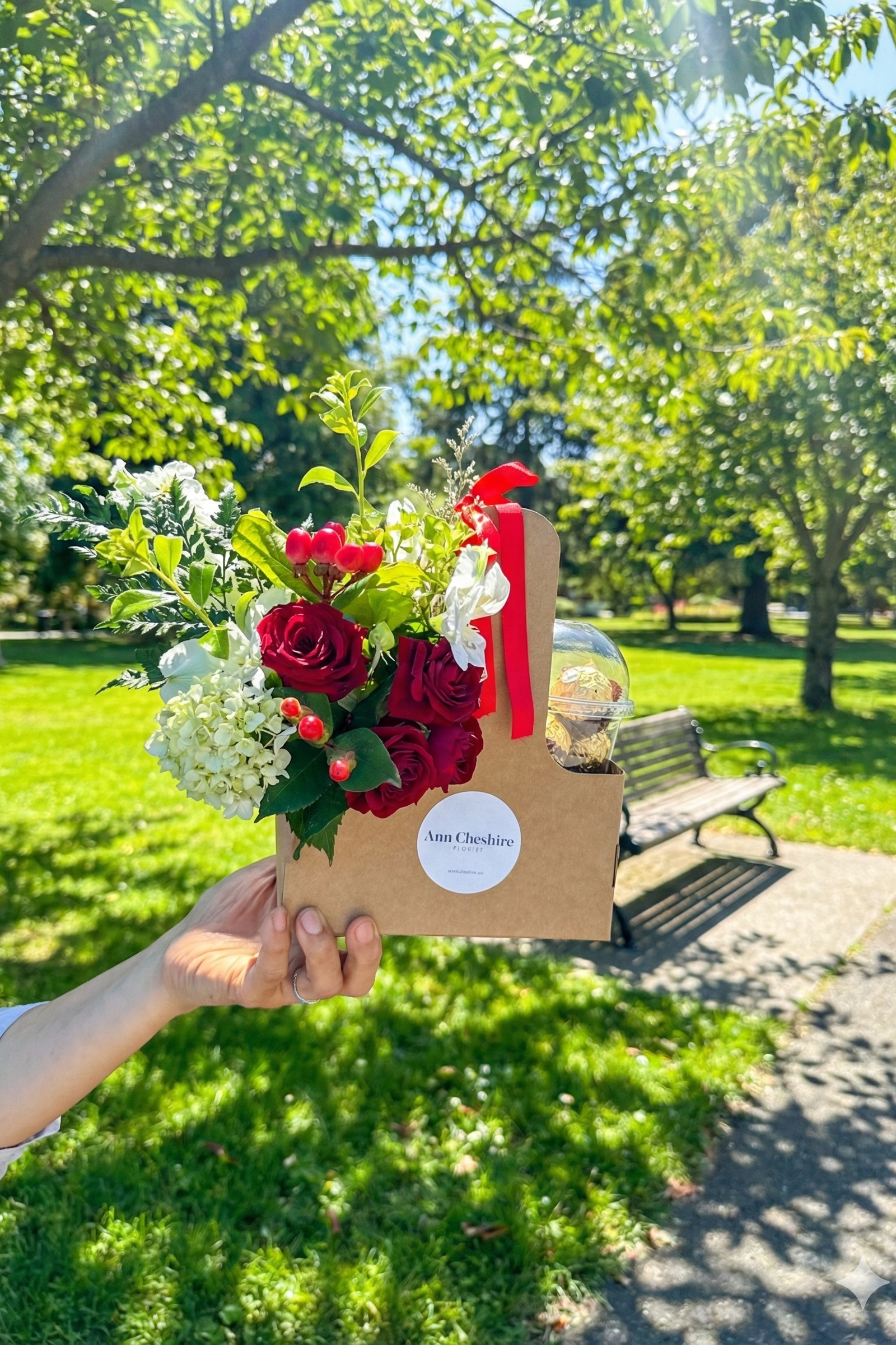 Bouquet of flowers in a cardboard box held by a person in a park.