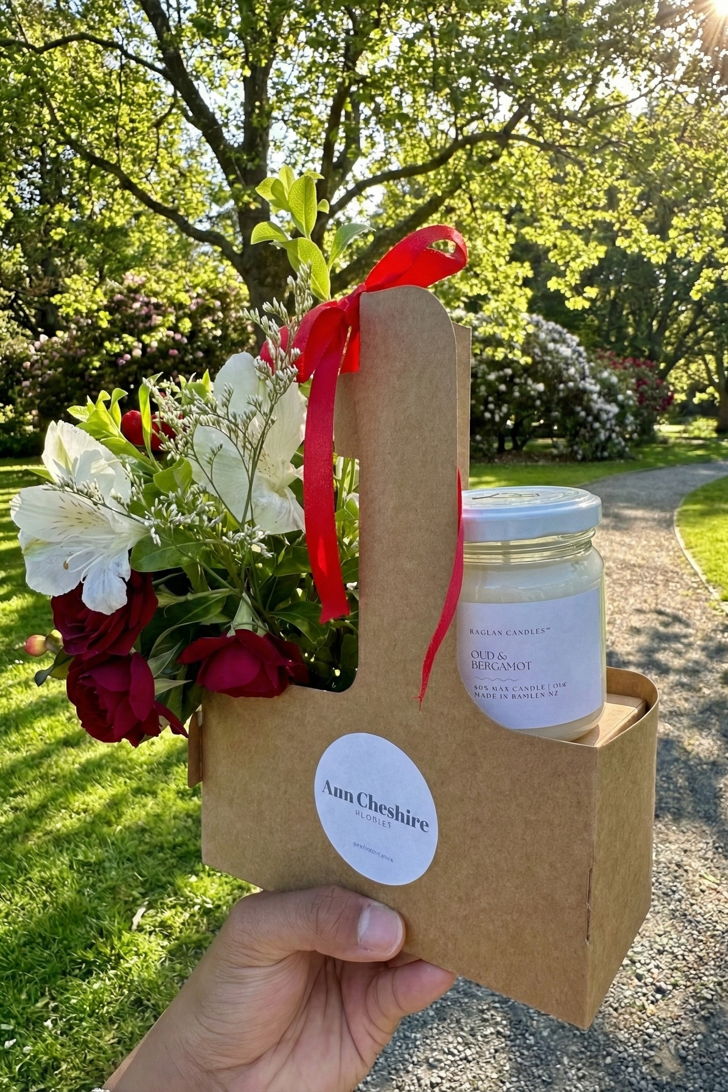 Hand holding a gift set with flowers and a candle in a natural setting