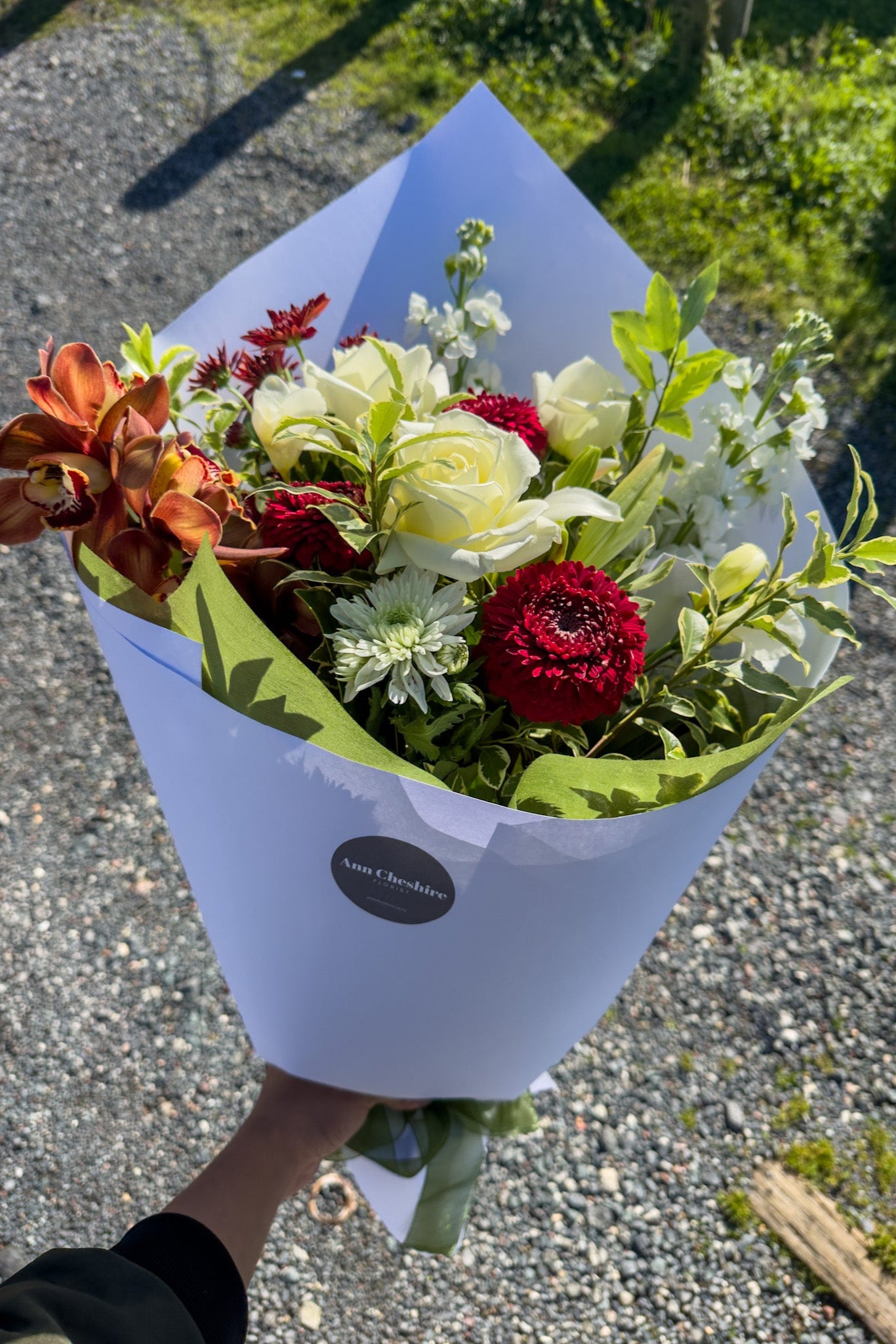 Bouquet of flowers wrapped in white paper held by a person outdoors.