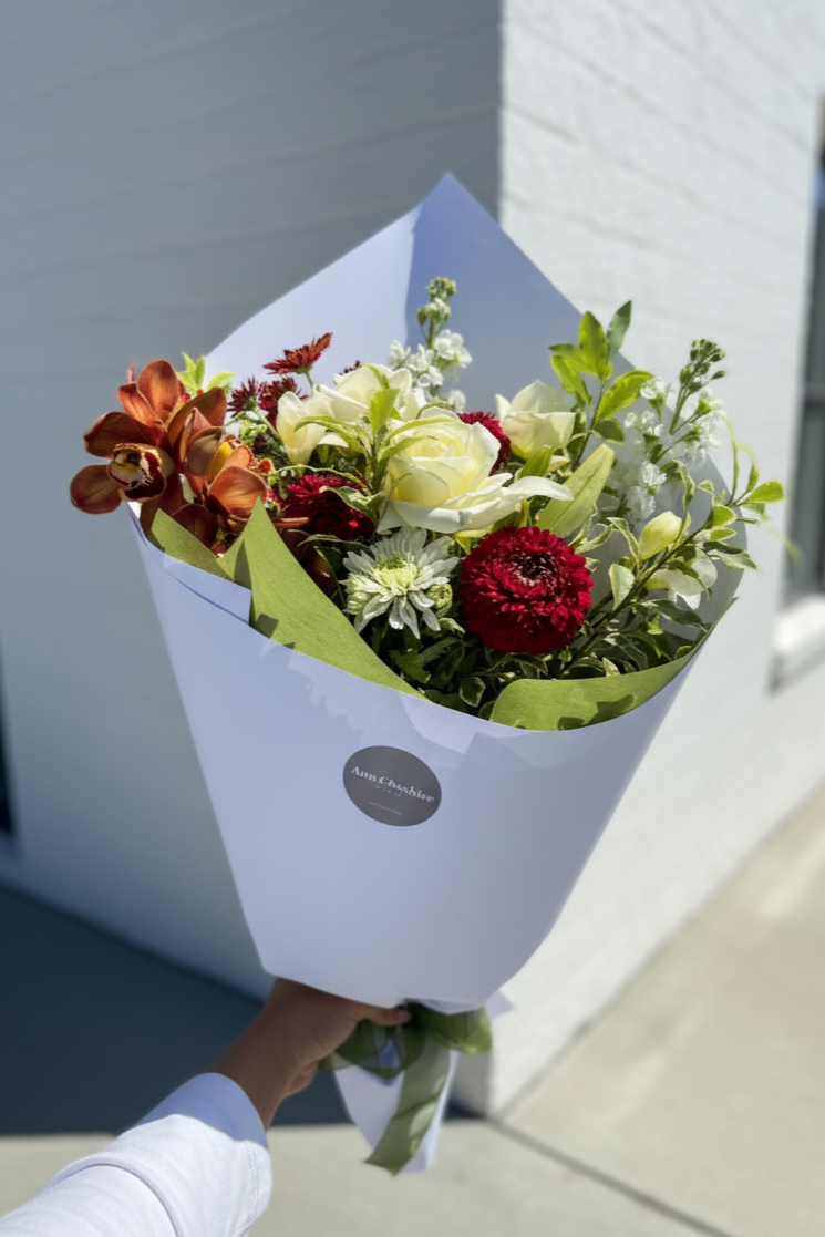 Bouquet of flowers wrapped in white paper held by a person against a building background