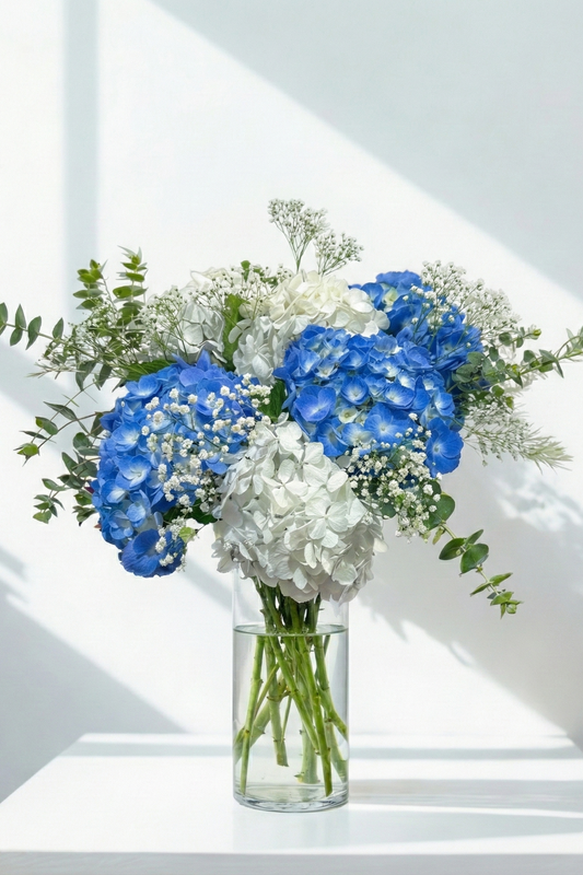 Bouquet of blue and white flowers in a clear vase on a white surface with light background