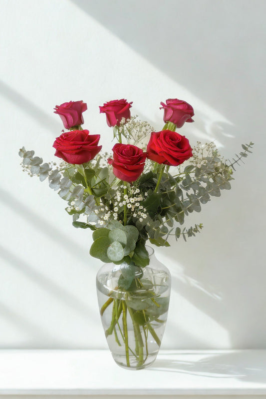 Bouquet of red roses in a clear vase on a white surface with a light background